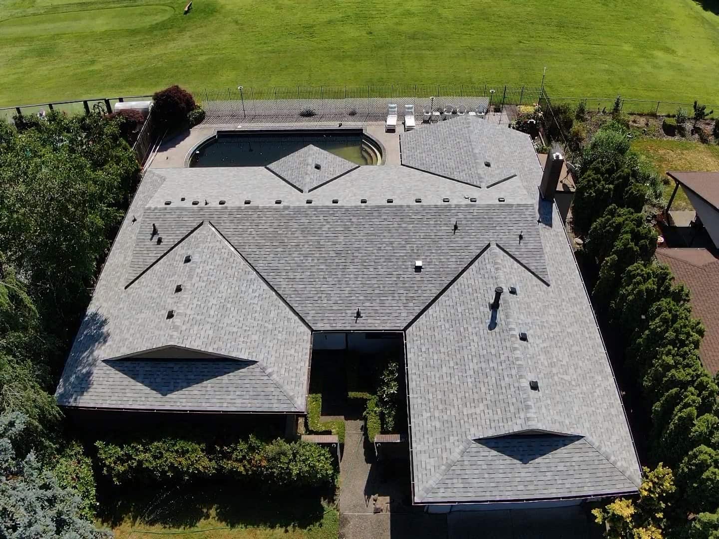 Aerial view of a large house with a gray roof, surrounding greenery, and a backyard pool.